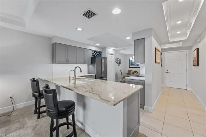 Kitchen featuring stainless steel fridge, sink, light stone countertops, and a raised ceiling