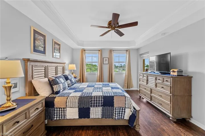 Bedroom with ornamental molding, ceiling fan, a raised ceiling, and dark wood-type flooring
