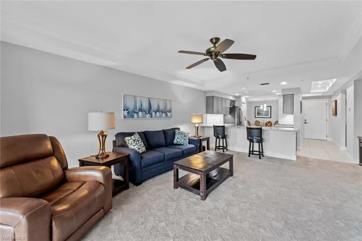 Carpeted living room featuring ceiling fan, crown molding, and a tray ceiling