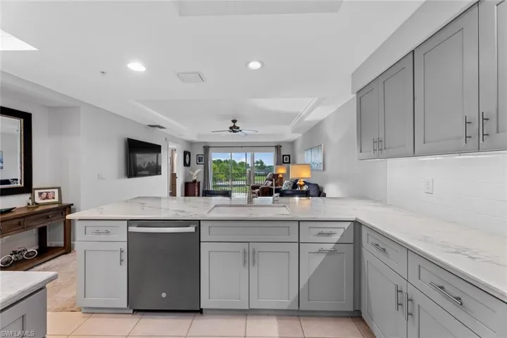 Kitchen with light tile patterned flooring, ceiling fan, sink, dishwasher, and a raised ceiling