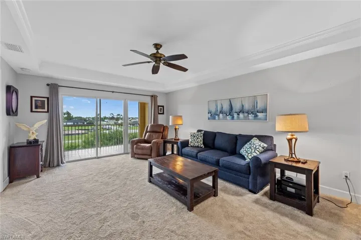 Carpeted living room featuring ceiling fan, crown molding, and a tray ceiling