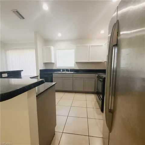 Kitchen featuring black appliances, gray cabinets, light tile patterned floors, recessed lighting, and white cabinetry