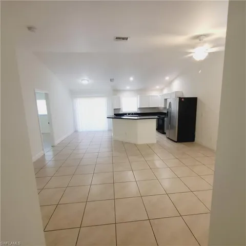 Kitchen with stainless steel fridge, light tile patterned floors, open floor plan, dark countertops, and recessed lighting