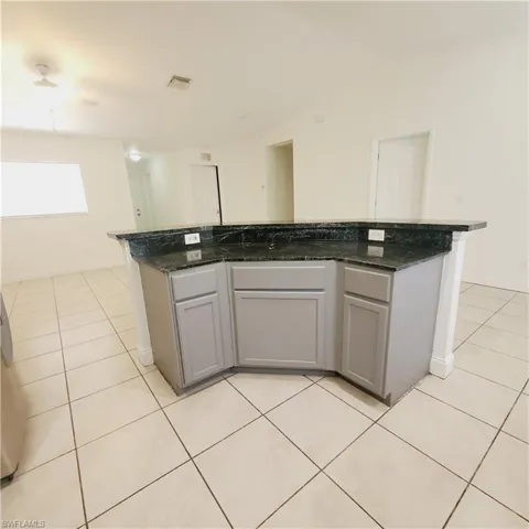 Kitchen featuring gray cabinets, a kitchen island, light tile patterned flooring, and dark stone counters