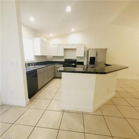 Kitchen featuring vaulted ceiling, black appliances, recessed lighting, light tile patterned floors, and white cabinetry
