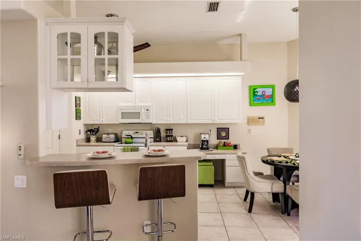 Kitchen with a breakfast bar, white appliances, lofted ceiling, white cabinets, and light tile patterned flooring