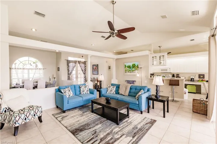Living room featuring ceiling fan, light tile patterned flooring, ornate columns, and vaulted ceiling