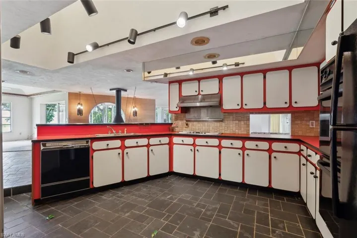 Kitchen with backsplash, dark tile patterned flooring, white cabinetry, dishwasher, and decorative light fixtures