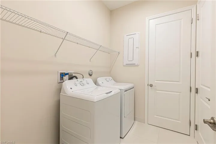 Laundry room with electric panel, tile patterned floors, and independent washer and dryer