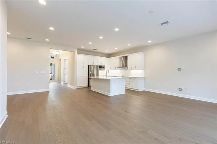 Kitchen with open floor plan, white cabinetry, a center island with sink, recessed lighting, and light wood finished floors