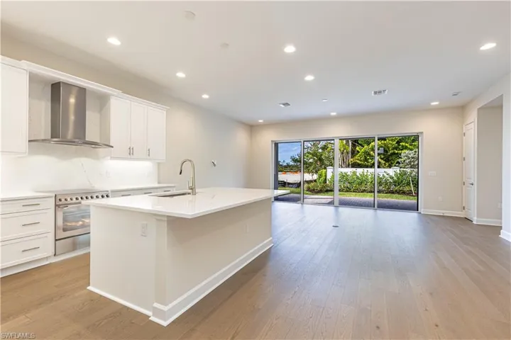 Kitchen featuring white cabinets, electric range, light wood-type flooring, recessed lighting, and an island with sink
