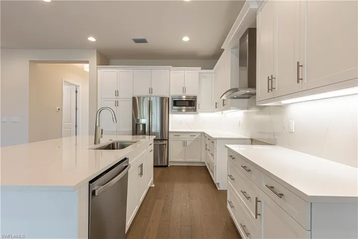 Kitchen with a center island with sink, white cabinets, stainless steel appliances, dark wood-style floors, and light stone counters