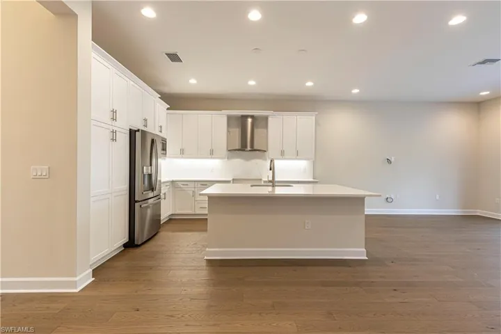 Kitchen featuring recessed lighting, stainless steel fridge with ice dispenser, white cabinets, an island with sink, and dark wood-style flooring