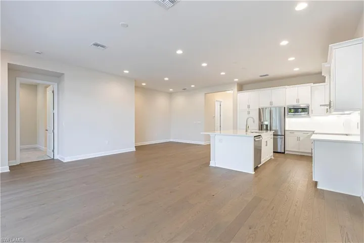 Kitchen featuring white cabinetry, stainless steel appliances, light wood finished floors, open floor plan, and a center island with sink