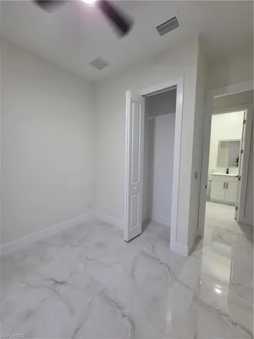 Unfurnished bedroom featuring light marble finish floors and a ceiling fan