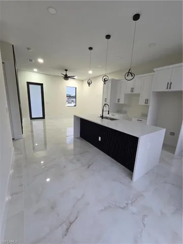 Kitchen featuring light stone counters, light marble finish flooring, a ceiling fan, recessed lighting, and white cabinetry