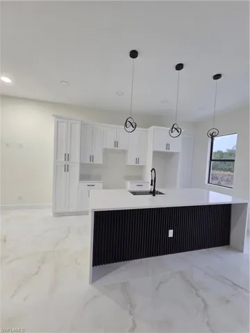 Kitchen featuring light stone countertops, a kitchen island with sink, decorative light fixtures, and recessed lighting