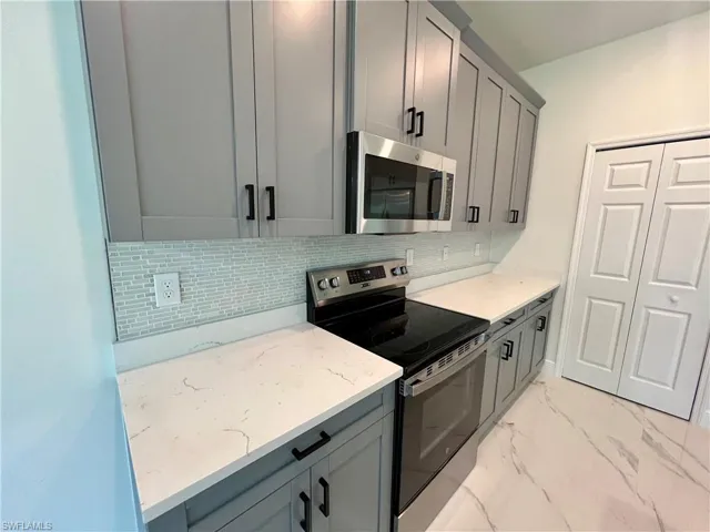 Kitchen featuring decorative backsplash, stainless steel appliances, gray cabinetry, and light QUARTZ countertops