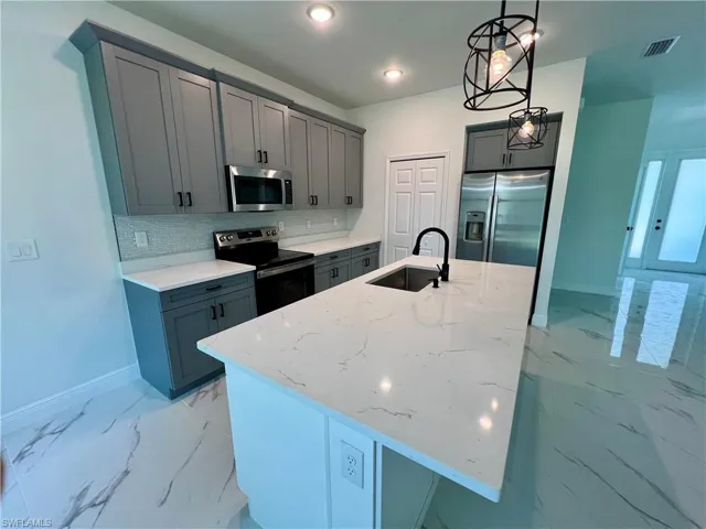 Kitchen featuring stainless steel appliances, sink, light QUARTZ counters, an island with sink, and pendant lighting