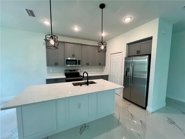 Kitchen with stainless steel appliances, QUARTZ counters, decorative light fixtures, and an island with sink