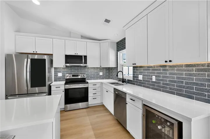 Kitchen with stainless steel appliances, lofted ceiling, light stone countertops, beverage cooler, and decorative backsplash