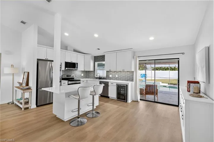 Kitchen featuring stainless steel appliances, a breakfast bar, white cabinets, tasteful backsplash, and recessed lighting