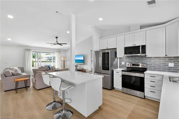 Kitchen with appliances with stainless steel finishes, white cabinetry, decorative backsplash, vaulted ceiling, and ceiling fan