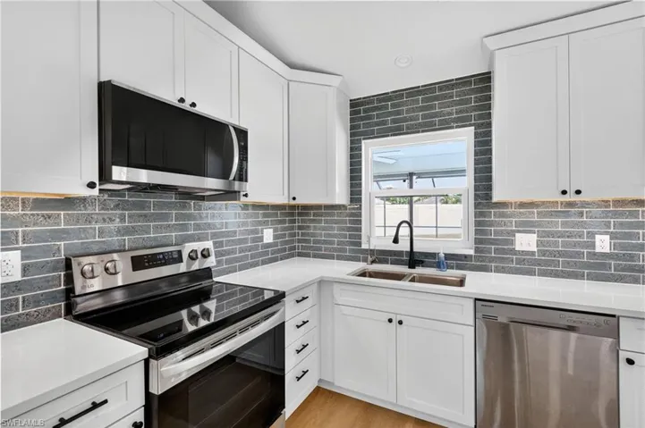 Kitchen with stainless steel appliances, white cabinetry, backsplash, light stone countertops, and light wood-type flooring