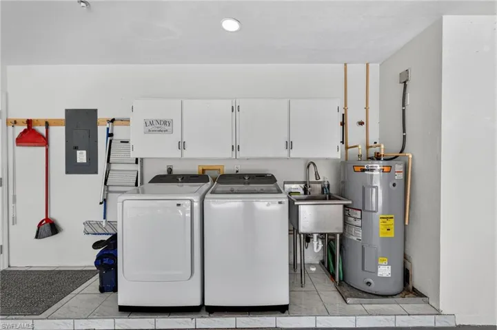 Laundry room with water heater, electric panel, cabinet space, washer and dryer, and light tile patterned floors