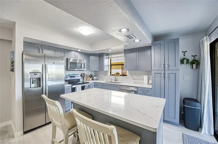 Kitchen with a kitchen breakfast bar, sink, light stone countertops, a kitchen island, and stainless steel appliances