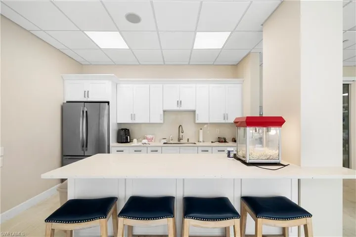Kitchen with a breakfast bar, a drop ceiling, white cabinets, light stone countertops, and tasteful backsplash