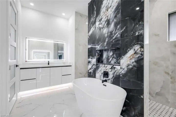 Full bath featuring marble tiled floors, a freestanding tub, vanity, a marble finish shower, and recessed lighting