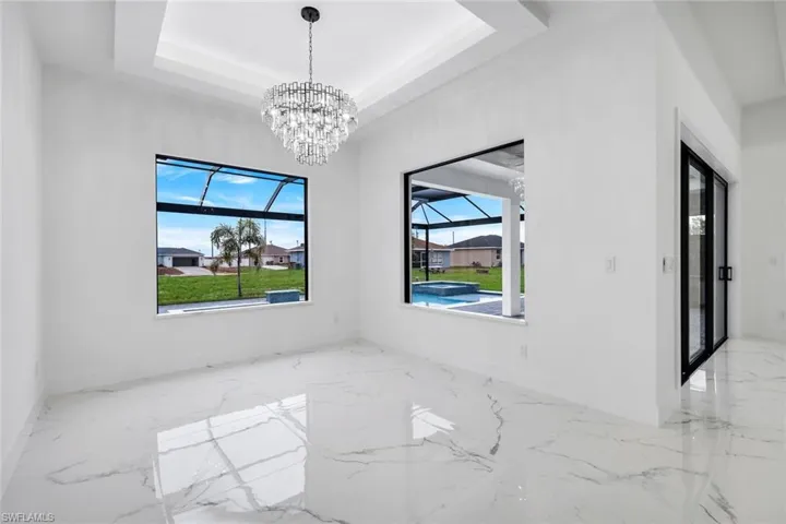 Empty room featuring light marble finish floors, a chandelier, a sunroom, and a raised ceiling