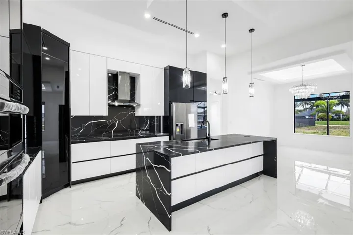 Kitchen with modern cabinets, decorative light fixtures, white cabinetry, an island with sink, and dark stone counters