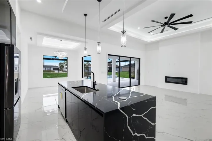 Kitchen with a tray ceiling, dark cabinets, modern cabinets, decorative light fixtures, and light marble finish flooring