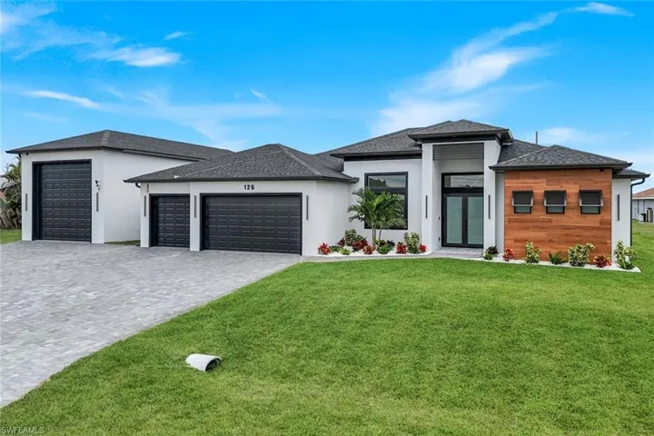 Prairie-style home featuring an attached garage, decorative driveway, a front lawn, stucco siding, and a shingled roof