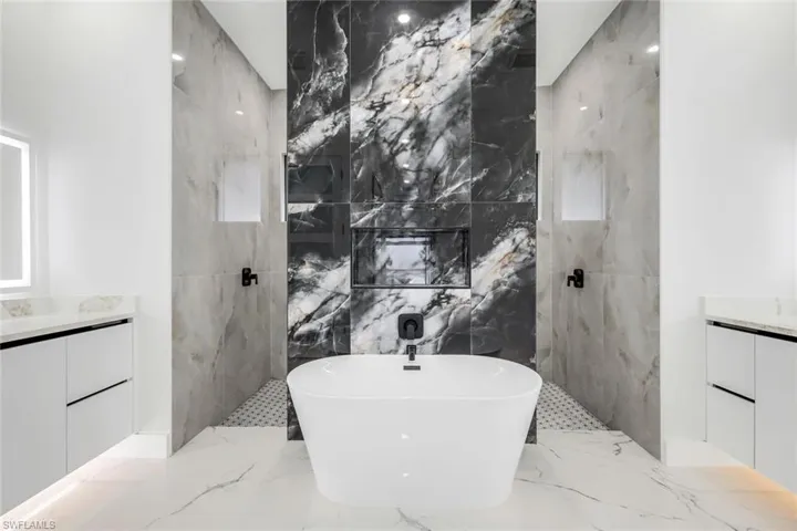 Full bath featuring light marble finish floors, a marble finish shower, vanity, and a freestanding bath