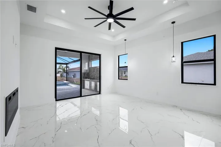 Unfurnished room featuring a sunroom, light marble finish flooring, ceiling fan, a tray ceiling, and recessed lighting
