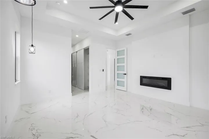 Unfurnished living room featuring a raised ceiling, a glass covered fireplace, recessed lighting, light marble finish flooring, and a ceiling fan