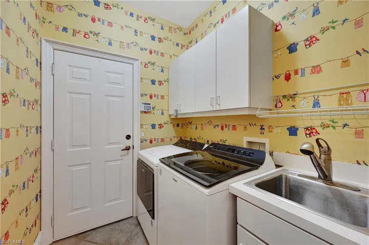 Laundry area with cabinets, light tile patterned flooring, washer and dryer, and sink