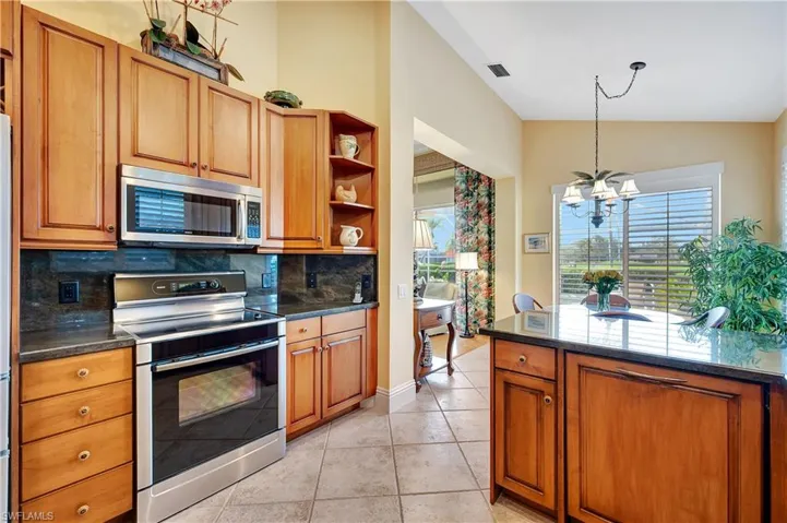 Kitchen with tasteful backsplash, a chandelier, vaulted ceiling, light tile patterned floors, and appliances with stainless steel finishes