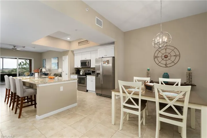 Kitchen with appliances with stainless steel finishes, a chandelier, white cabinets, light tile patterned floors, and a breakfast bar area