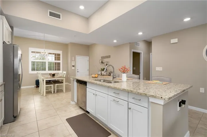 Kitchen featuring appliances with stainless steel finishes, light tile patterned floors, white cabinetry, a kitchen island with sink, and light stone countertops