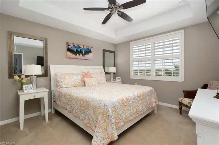 Carpeted bedroom featuring a raised ceiling and a ceiling fan