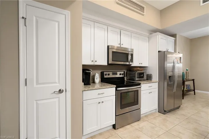 Kitchen with stainless steel appliances, light tile patterned floors, white cabinets, and light stone counters