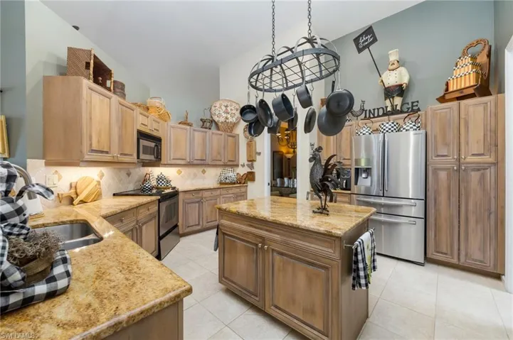 Kitchen featuring light stone countertops, a center island, stainless steel fridge with ice dispenser, range with electric stovetop, and light tile patterned floors