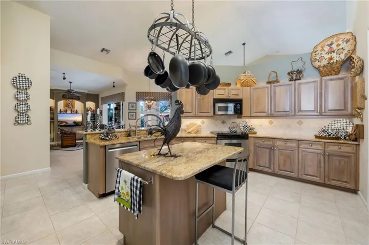Kitchen featuring a peninsula, a breakfast bar area, light stone counters, stainless steel appliances, and vaulted ceiling
