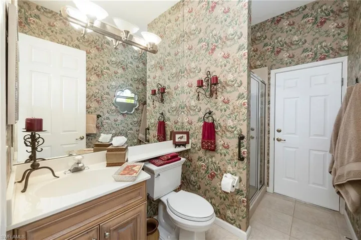 Bathroom featuring wallpapered walls, vanity, light tile patterned floors, a shower stall, and hanging lights