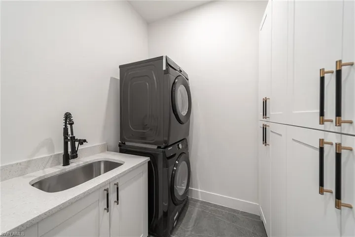 Washroom with sink, dark tile patterned floors, cabinets, and stacked washer and clothes dryer