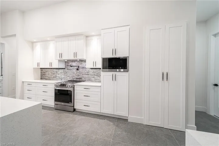 Kitchen featuring decorative backsplash, stainless steel range, built in microwave, a high ceiling, and white cabinetry